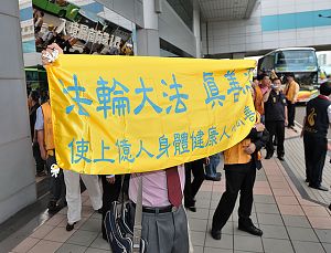 一位法轮功学员在中国武汉团的车子的正前方,将“法轮大法真善忍使上亿人身心健康”的横幅拉开