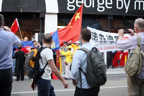 在悉尼主街乔治街上,亲共暴徒抢夺法轮功横幅。路过的澳洲民众纷纷拍照,并谴责暴徒的行径。