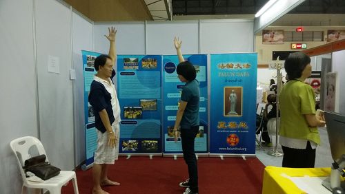 泰国健康与美容展上,参观者向法轮功学员学炼功法