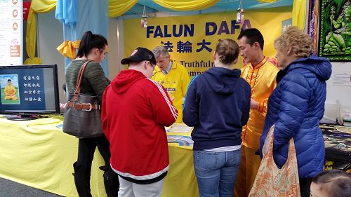 '图2:参加健康展的民众在法轮功摊位前驻足聆听真相。'