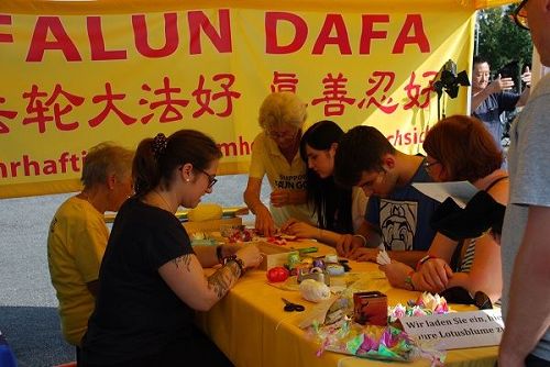 '图5:游客们在法轮功的展位上学习折莲花。'