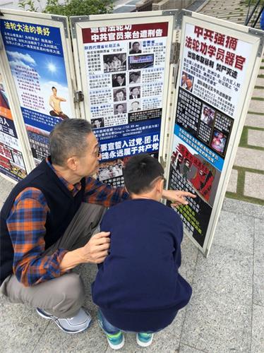'图6:这位游客听完法轮功学员讲真相后,带着孩子来到展板面前,给孩子讲起真相来。'