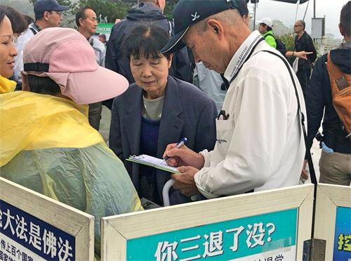 '图7~8:法轮功学员(穿雨衣者)向游客讲述真相,征集联署,游客签名声援法轮功反迫害。'