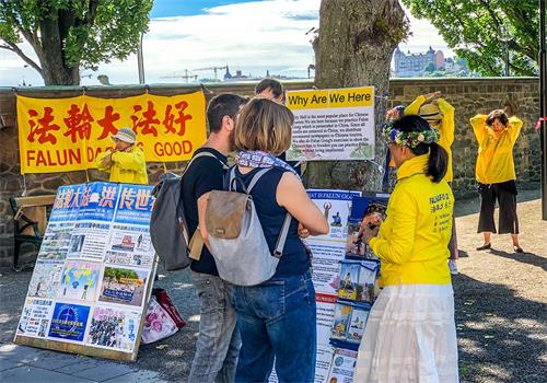 '图1~2:仲夏节期间法轮功学员头戴花环人们展示舒缓祥和的法轮功的五套功法,发放真相资料的学员带着微笑向游客送上节日的祝福。'