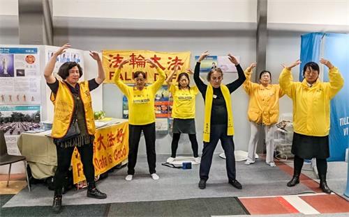 '图1:法轮功学员在展台前伴随着优美的炼功音乐向人们演示功法并现场教功。'