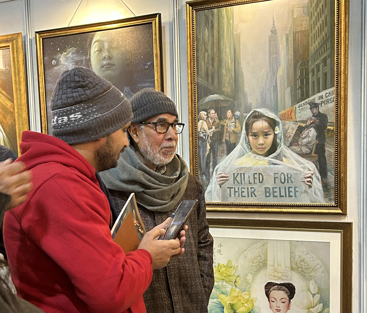 图9:资深印地语记者拉姆·巴哈杜尔·拉伊(右)在德里真善忍美展展位上听学员解释艺术作品。