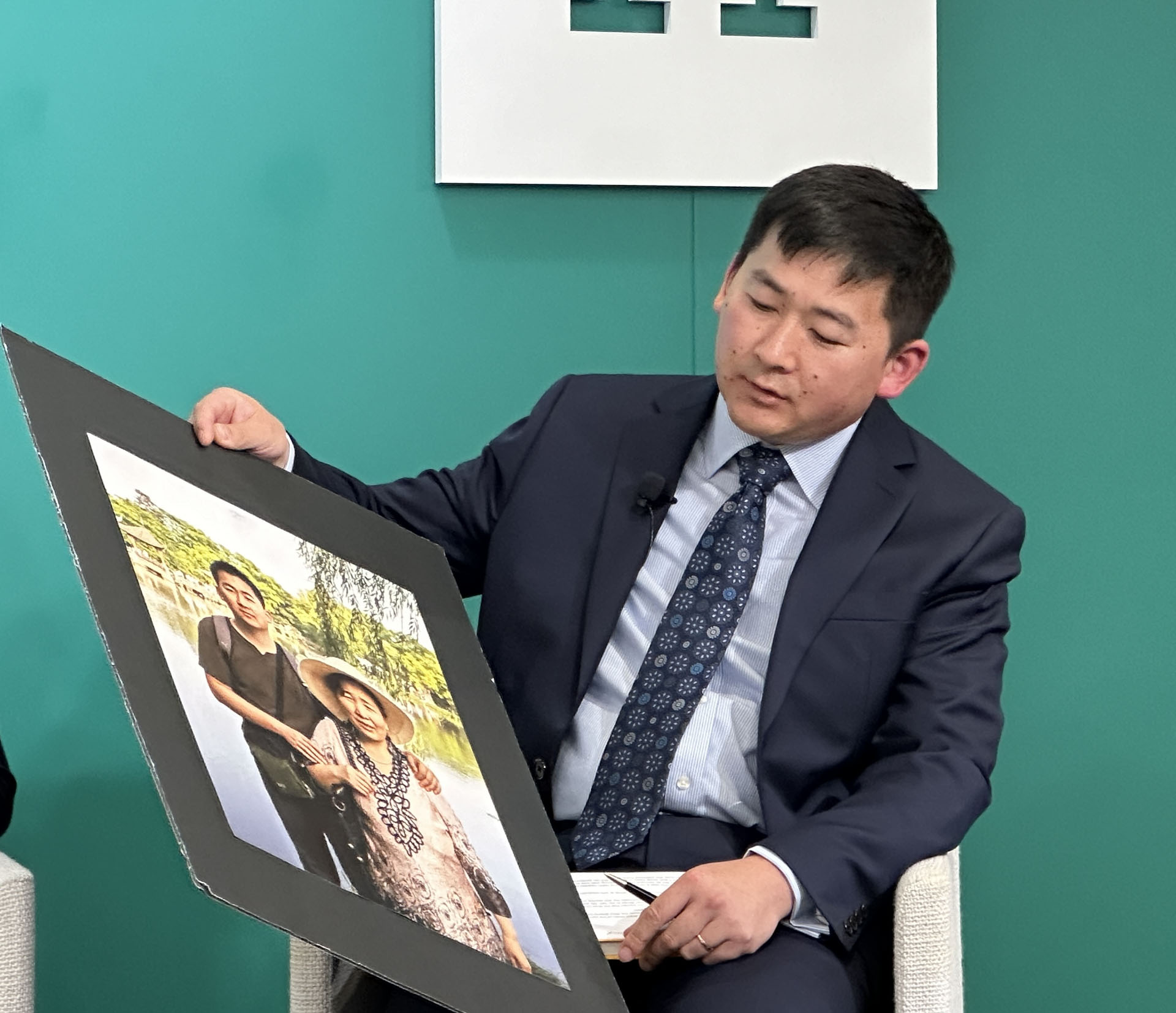 图4:二零二四年七月十七日,美国纽约布鲁克林的建筑师西蒙·张(Simon Zhang)在美国智库哈德逊研究所研讨会现场,向观众展示他和母亲季云芝在二零一二年的合影。